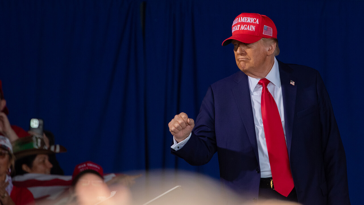 Donald J. Trump pokes outside bulletproof glass to pump his fist.