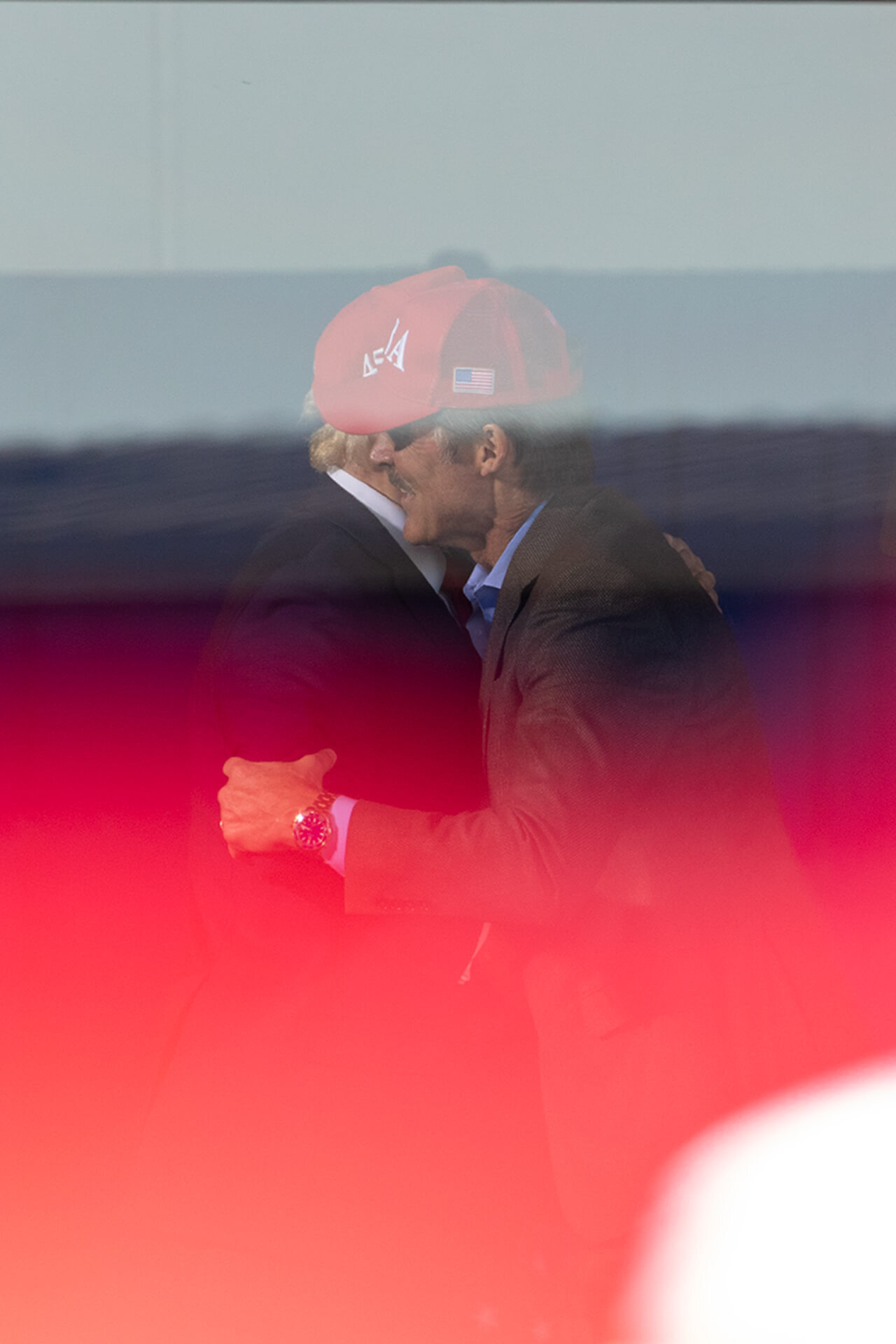 Eric Hovde embraces Donald Trump behind reflective ballistic glass.