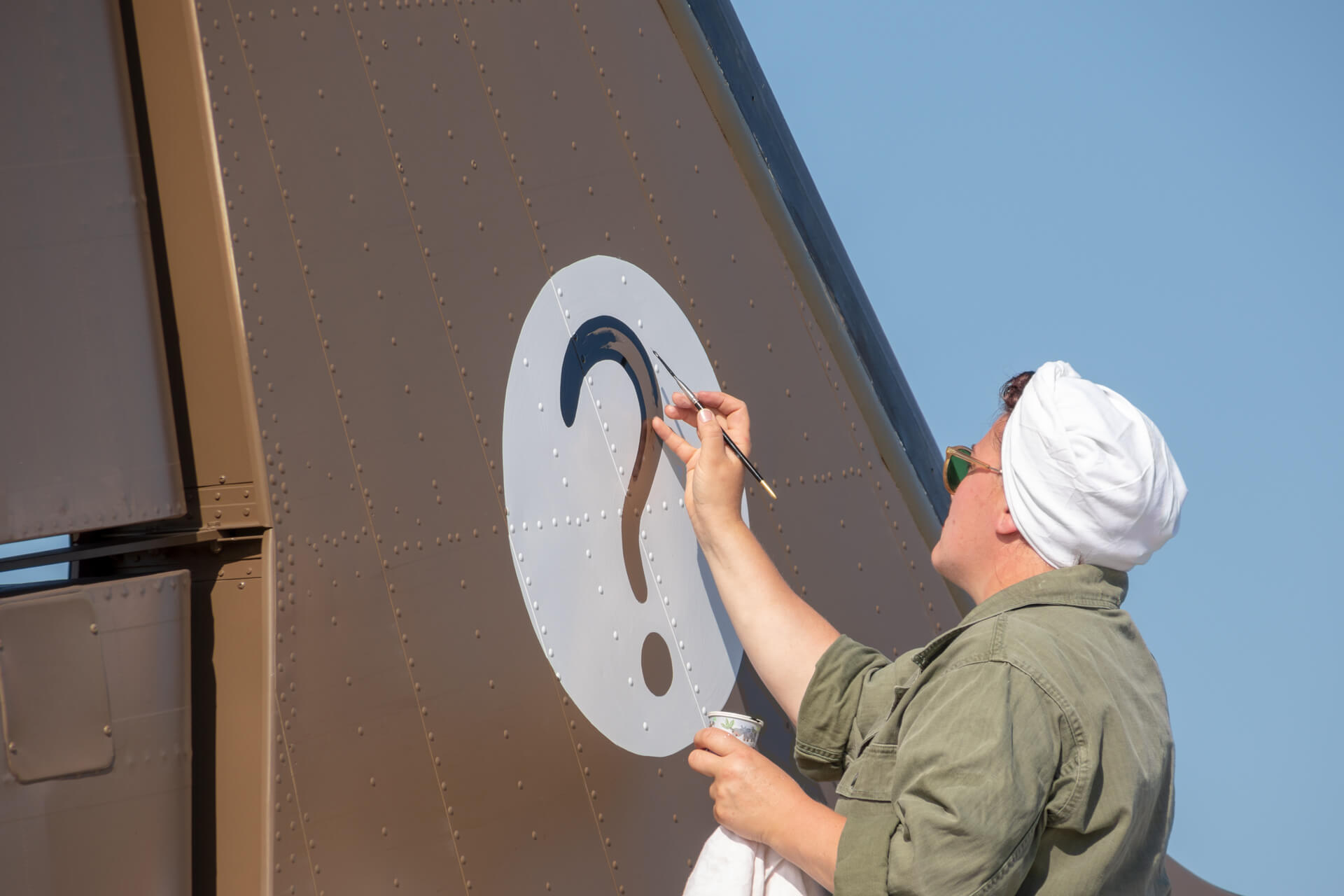 A women paints the 319th Troop Carrier Squadron insignia (a question mark) on the vertical stabilizer of ‘Hairless Joe’, a Douglas C-47 Skytrain.