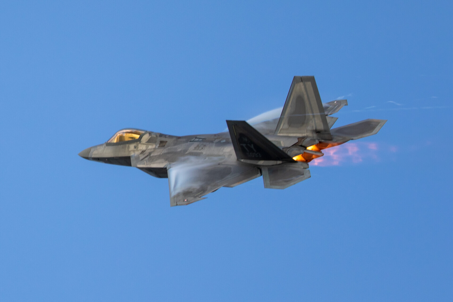 The pressure differentiation produced by the exhaust of the afterburners causes pulsating orange “Shock Diamonds” to stream behind the F-22.