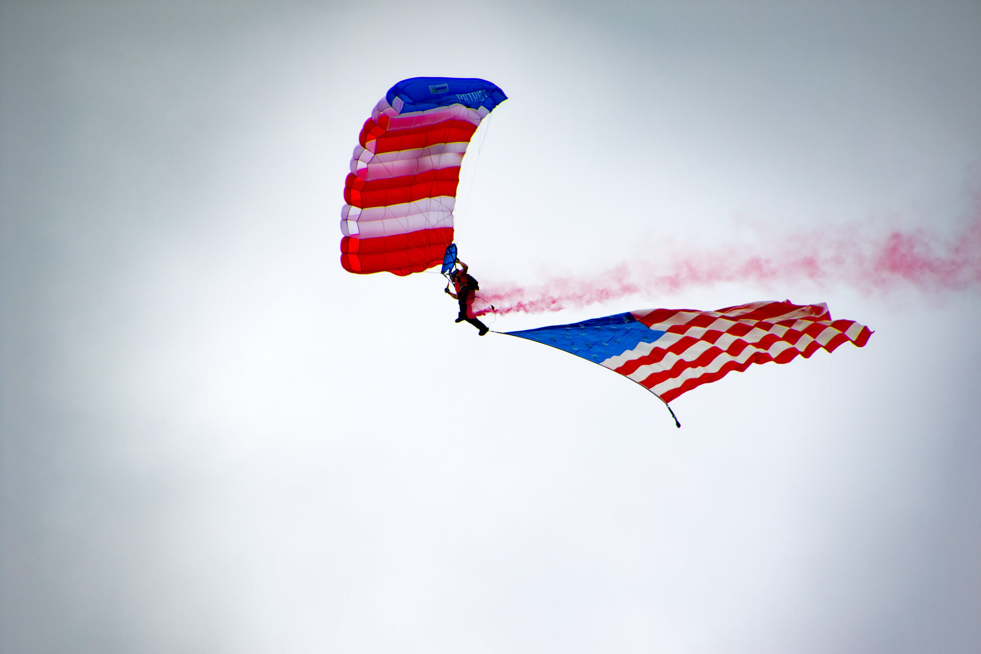 Parashooting team glides down with Old Glory during the national anthem to start the AirVenture airshow.